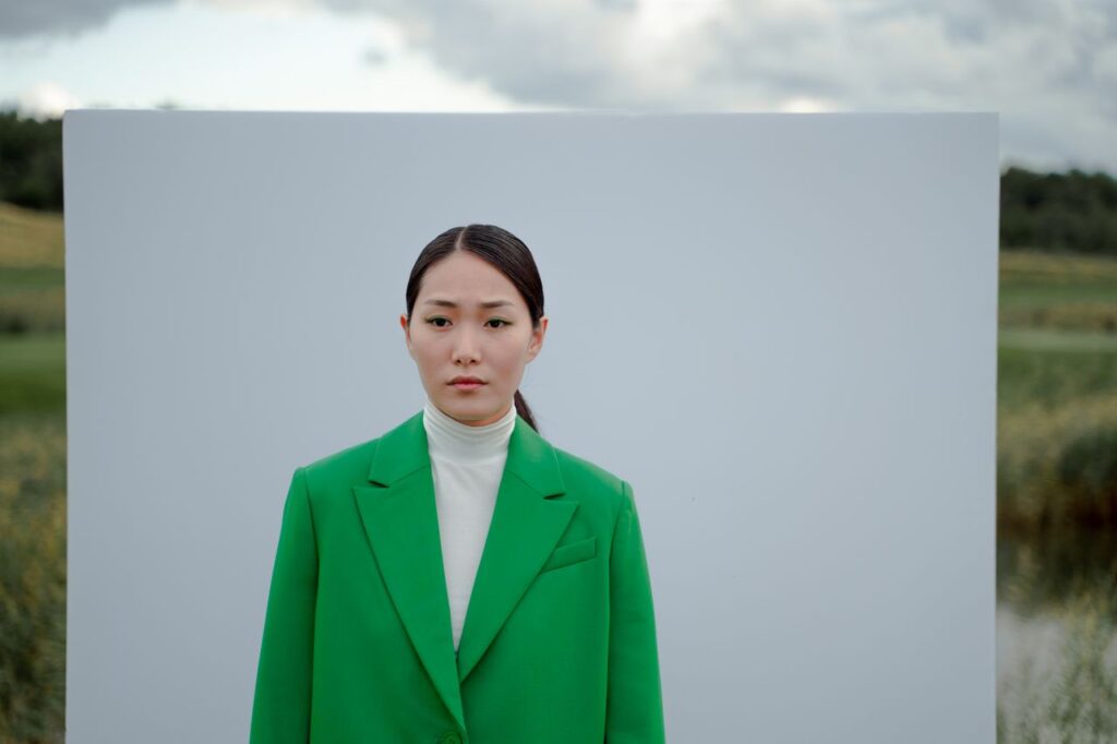 A contemplative woman in an eye-catching green blazer against an outdoor backdrop, highlighting modern fashion.