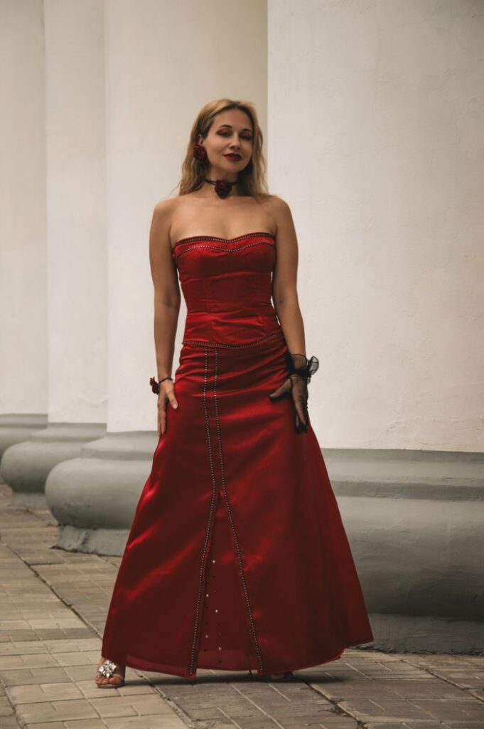A woman in a strapless red dress stands elegantly outdoors.