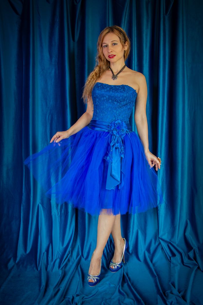 Woman elegantly posing in a strapless blue dress with a draped fabric background.